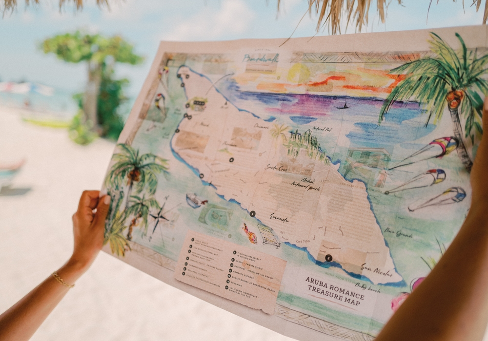 Hands holding a colorful illustrated map of Aruba titled 'Aruba Romance Treasure Map' at Boardwalk Boutique Hotel