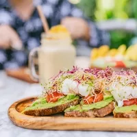 Avocado toast with poached eggs and microgreens served on a wooden board at Coco Café, with a smoothie in the background